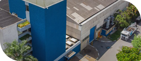 Empresa Toledo do Brasil, possui estrutura robusta cinza e azul, arvores na frente, pilar azul a esquerda e caminhão passando na frente