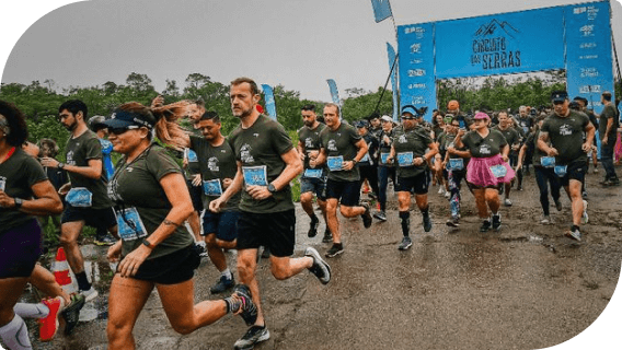 Imagens composta por participantes na corrida desafio da serra, com camiseta verde e short preto e ao fundo placa de largada azul