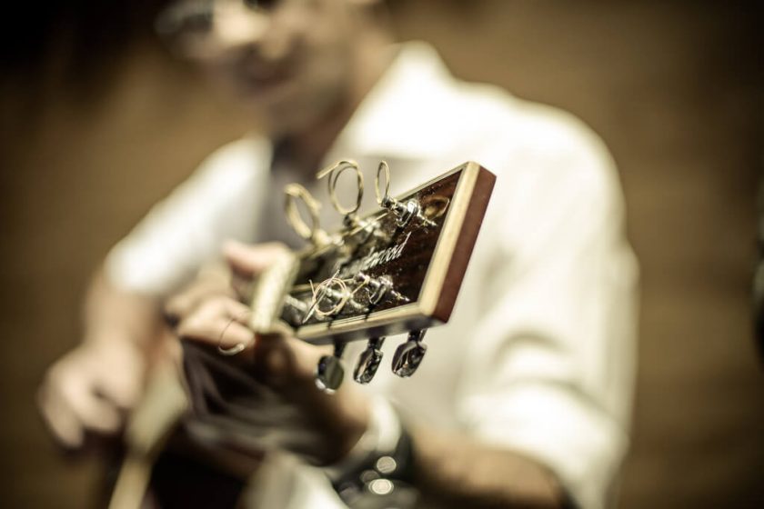 Close em músico tocando violão com foco nas tarraxas do instrumento durante apresentação no Festival de Música da Toledo do Brasil.