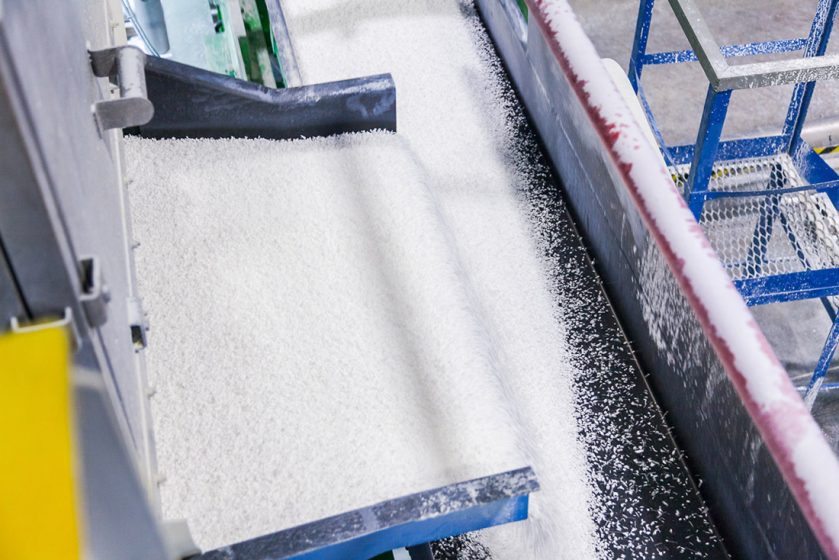 Açúcar branco sendo transportado em uma correia industrial dentro de usina de produção.